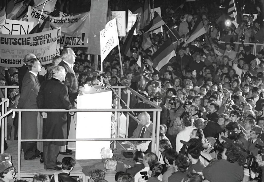 - Bundesarchiv 1989 Dresden Kohl Rede auf Altmarkt 1 elmut Kohl à Dresde le 19 décembre 1989 sur le Altmarkt — Devant une foule immense, les pancartes proclament « Dresde salue le chancelier » : c’est ici, la veille de l’arrivée de Mitterrand en RDA, que Kohl prononce pour la première fois le mot « unité » — Photo © Bundesarchiv