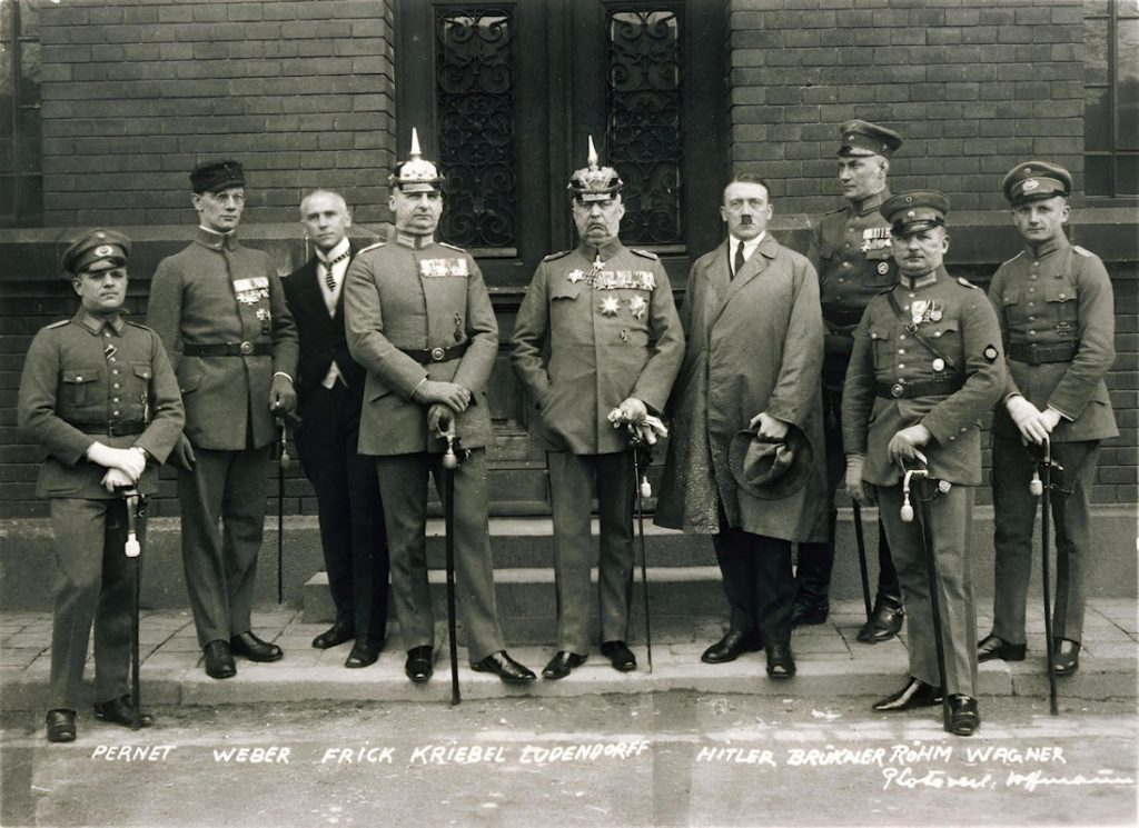 - Bundesarchiv Munchen nach Hitler Ludendorff Prozess 1a Hitler et ses co-accusés dans la cour du tribunal de Munich, le 1er avril 1924, avant l'annonce du verdict du procès pour le putsch manqué de la Brasserie (novembre 1923). La clémence du jugement — cinq ans de forteresse dont Hitler n'en purgera que neuf mois — scandalisa les observateurs de l'époque et lui permit de transformer le procès en tribune politique — Photo Heinrich Hoffmann / Bundesarchiv