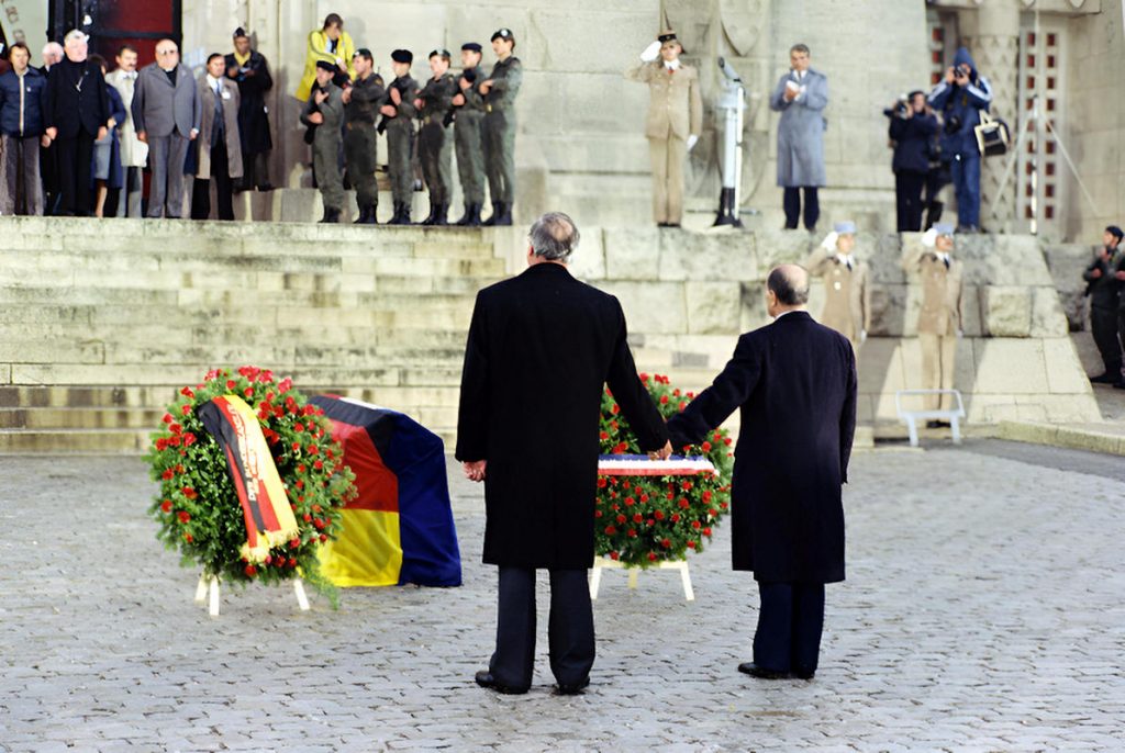 - Kohl Mitterand Verdun Bundesregierung Ulrich Wienke Helmut Kohl et François Mitterrand devant l’ossuaire de Douaumont, Verdun, 22 septembre 1984 — recueillis, la main de l’un posée sur celle de l’autre, face aux gerbes tricolores et aux couleurs allemandes — Photo Bundes-regierung © Ulrich Wienke