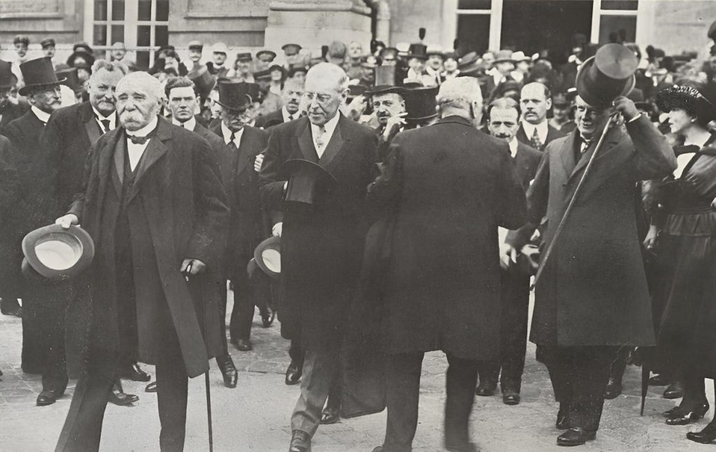 - Versailles 1919a Georges Clemenceau (au premier plan) et Woodrow Wilson quittent le palais de Versailles, le 28 juin 1919, jour de la signature du traité. Deux des trois artisans du « Big Three » — avec David Lloyd George — qui ont imposé à l'Allemagne vaincue les termes d'une paix que Clemenceau lui-même jugeait déjà trop indulgente, et que les Allemands, eux, jugeront impitoyable — Photo Keystone (Domaine public)